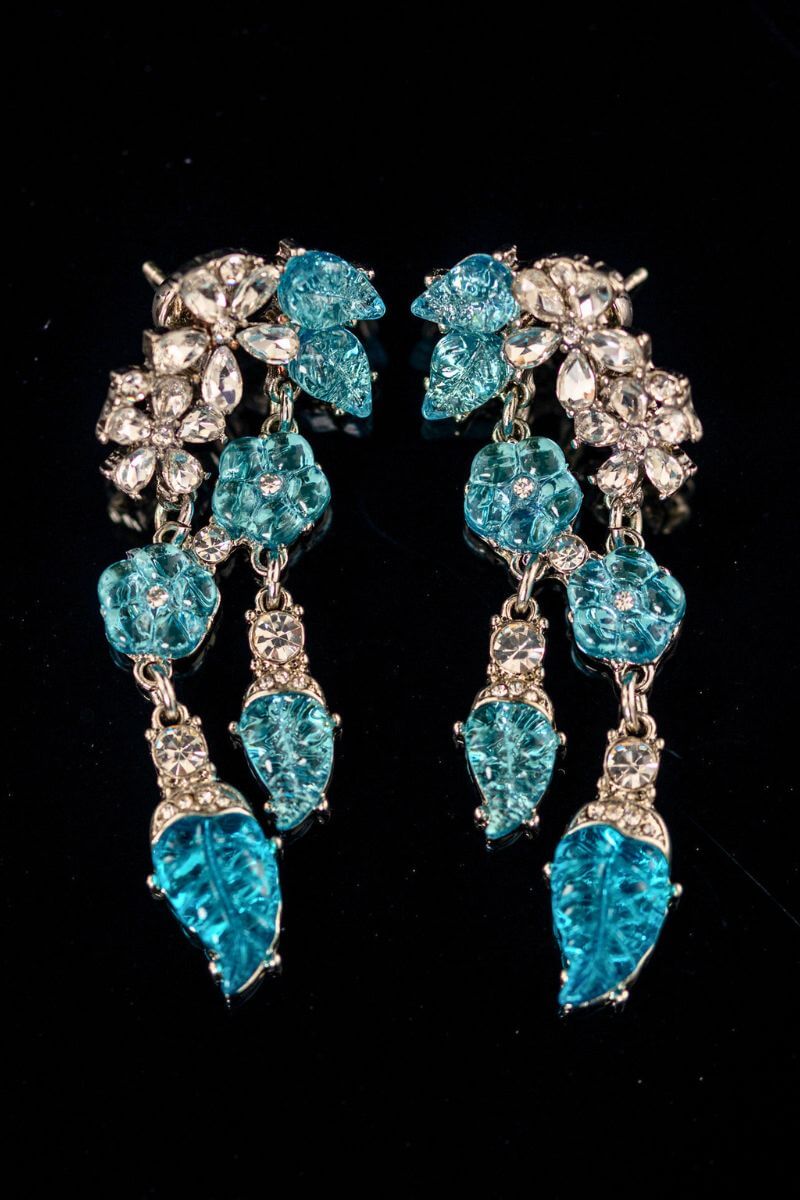 A pair of aqua blue crystal drop earrings with leaf-shaped stones and clear crystal accents, arranged symmetrically on a black reflective surface.