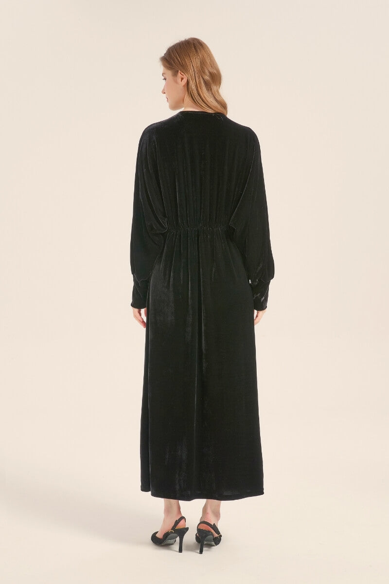 Back view of model wearing a long black velvet dress with elastic waist and full-length drape.