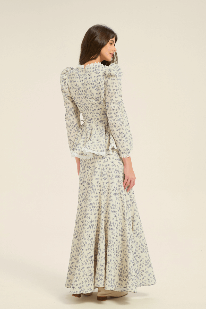 Model showing the back of the cream and blue floral two-piece set with long-sleeve peplum blouse and maxi skirt.