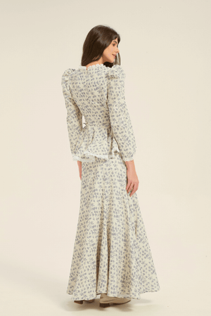 Model showing the back of the cream and blue floral two-piece set with long-sleeve peplum blouse and maxi skirt.