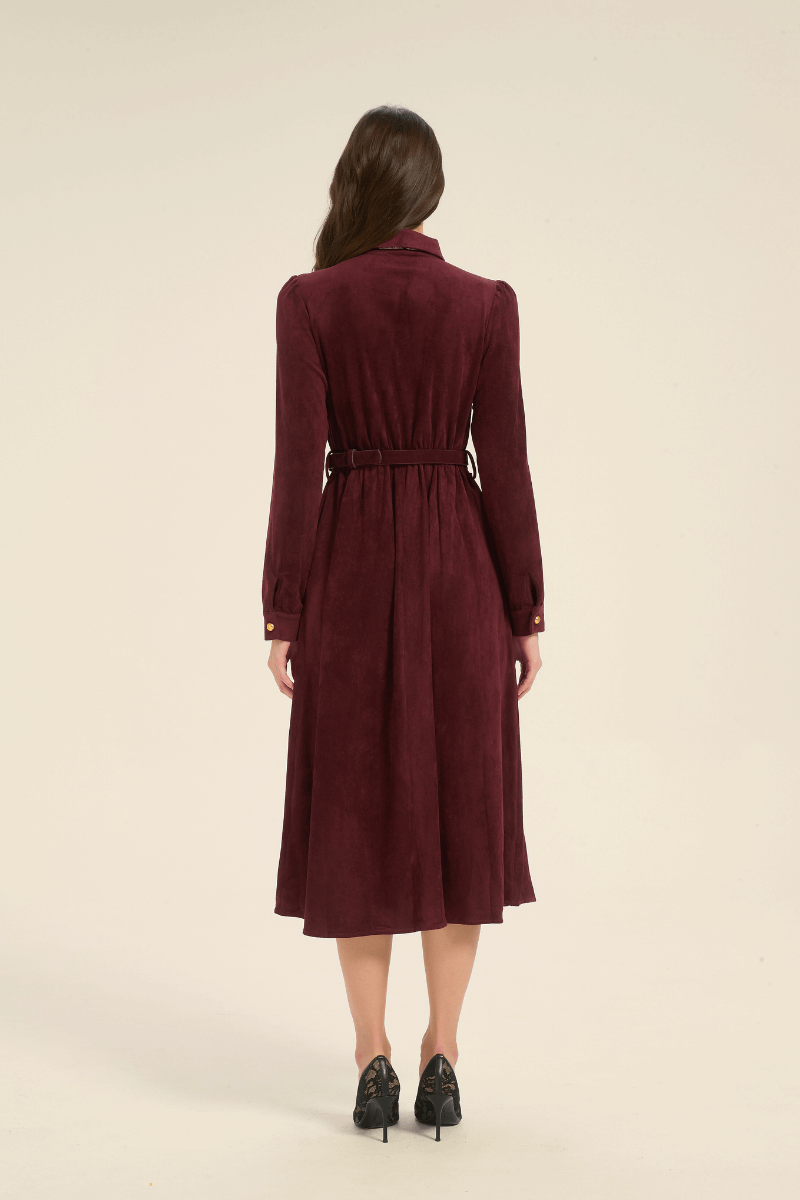 Rear view of a model wearing a long-sleeve burgundy midi dress with a belted waist and collared neckline, styled with black lace heels.