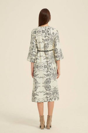Model shown from the back wearing a cream midi dress with black botanical print, 3/4 sleeves, and slim black belt.