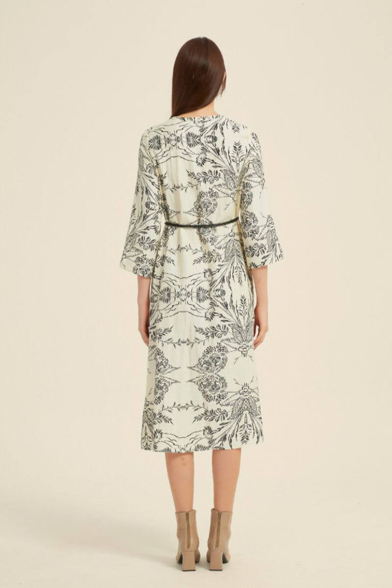 Model shown from the back wearing a cream midi dress with black botanical print, 3/4 sleeves, and slim black belt.