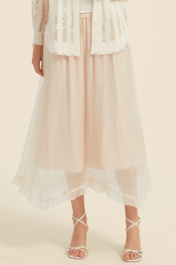 Back view of a model in an ivory sheer stripe embroidered blouse and layered blush midi skirt with soft pleats and flowy hemline.