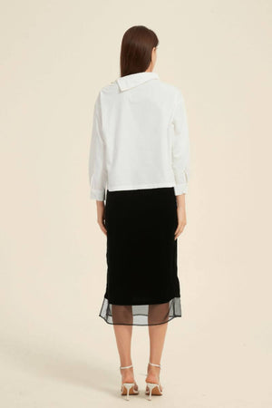 Rear view of a white asymmetric-collar blouse paired with a black midi skirt featuring a sheer hem — minimalist monochrome outfit by Sioéne.