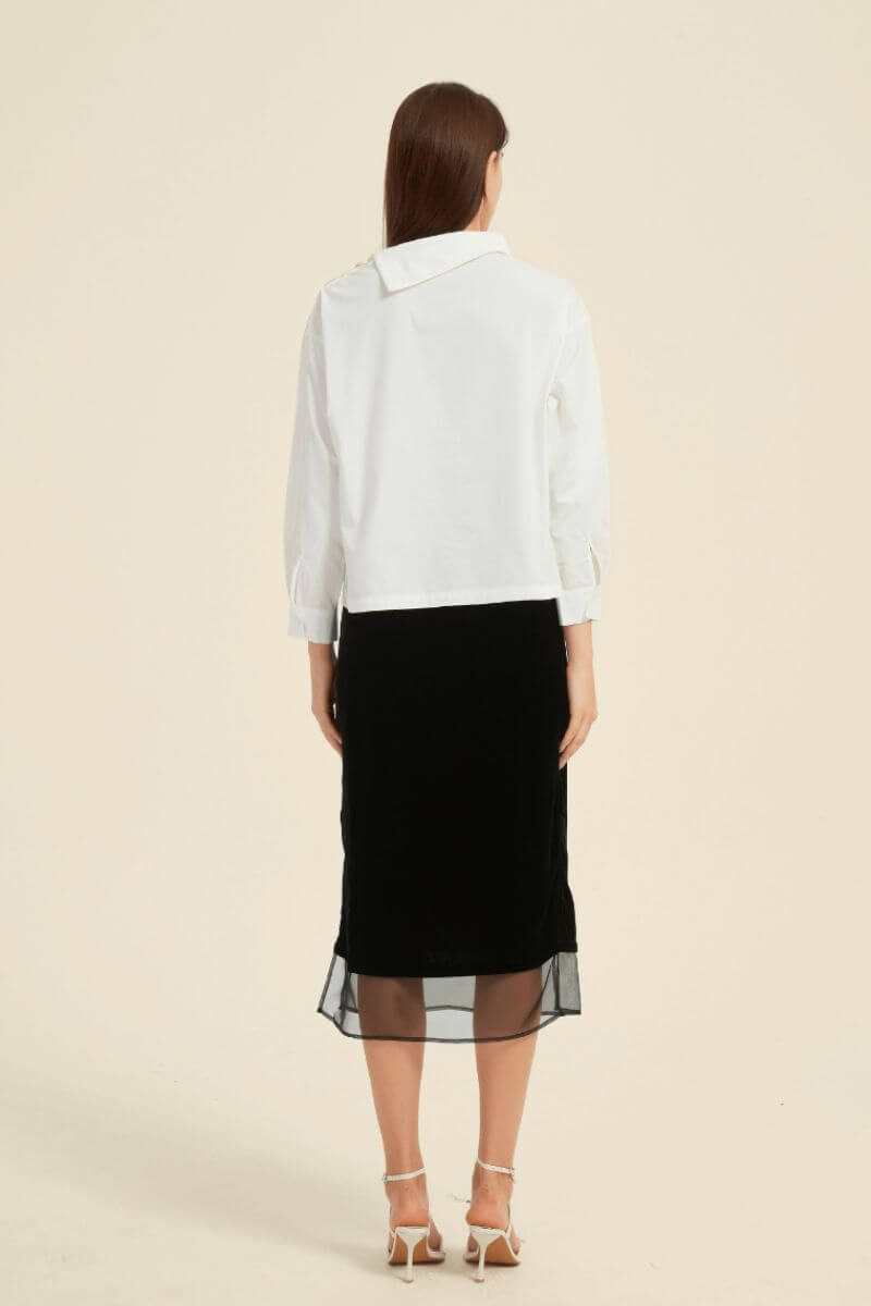 Rear view of a white asymmetric-collar blouse paired with a black midi skirt featuring a sheer hem — minimalist monochrome outfit by Sioéne.