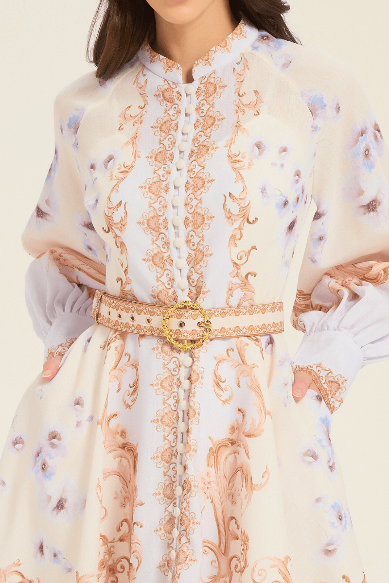Close-up of front detail on cream mini dress with ornate golden scroll print, fabric buttons, and a matching belt with gold buckle.