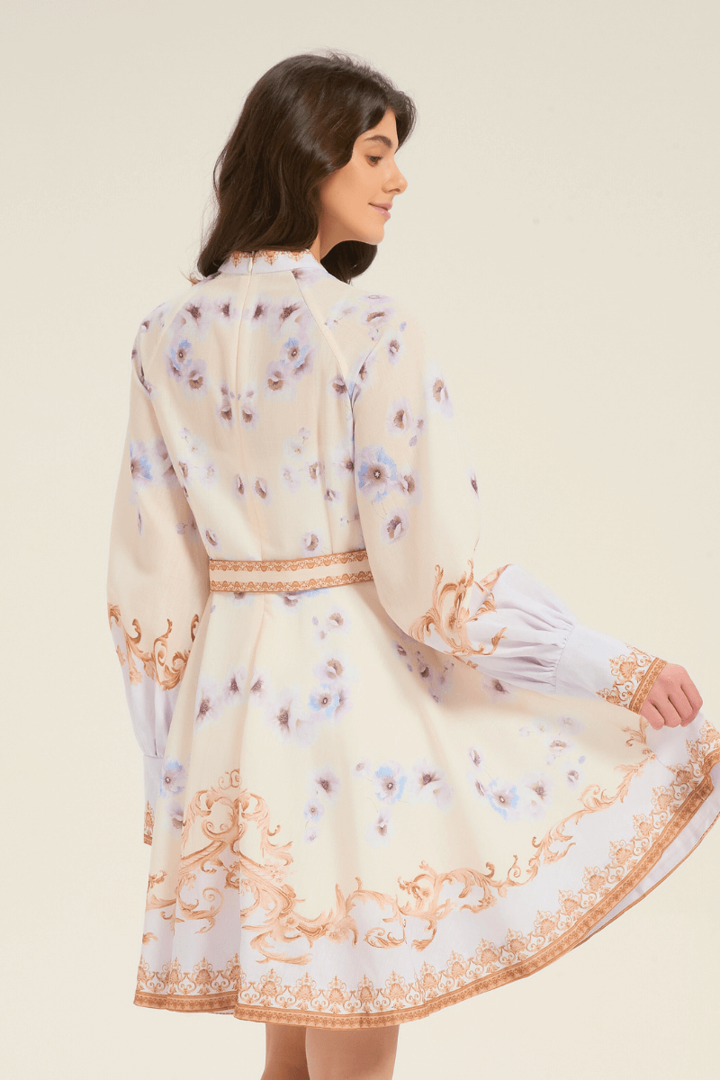 Back view of cream mini dress with golden baroque scrolls and blue floral print, showing long puff sleeves and flared skirt in motion.