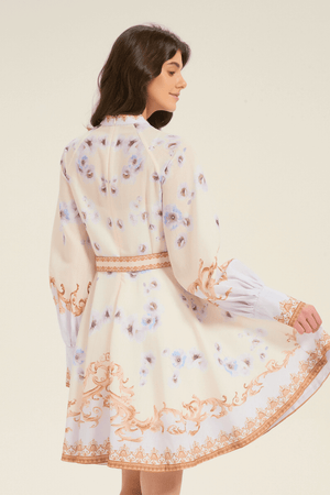 Back view of cream mini dress with golden baroque scrolls and blue floral print, showing long puff sleeves and flared skirt in motion.