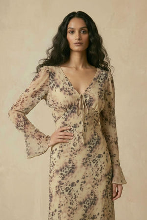 A woman wearing a beige animal-print chiffon midi dress with a V-neck, tie-front detail, and flared sleeves, shown from an angled front view.