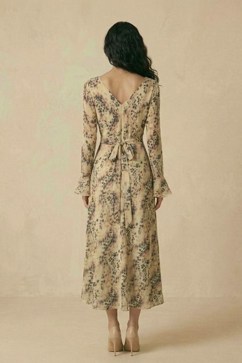 A woman shown from the back wearing a beige animal-print chiffon midi dress with a V-shaped back neckline and a self-tie waist ribbon.