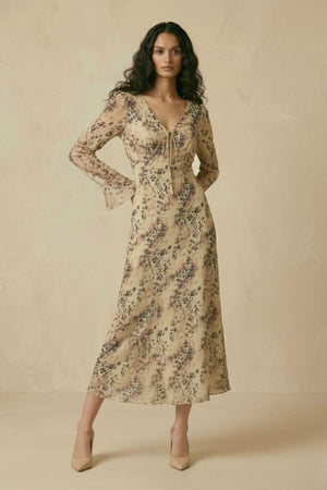 A woman wearing a beige animal-print chiffon midi dress with a V-neckline, long sleeves, and a flowing A-line skirt, shown in a full front view.