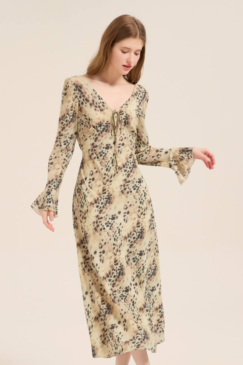 Model wearing a lightweight beige leopard print midi dress featuring a deep V-neck and tie detail, long sleeves, and a fluid silhouette.