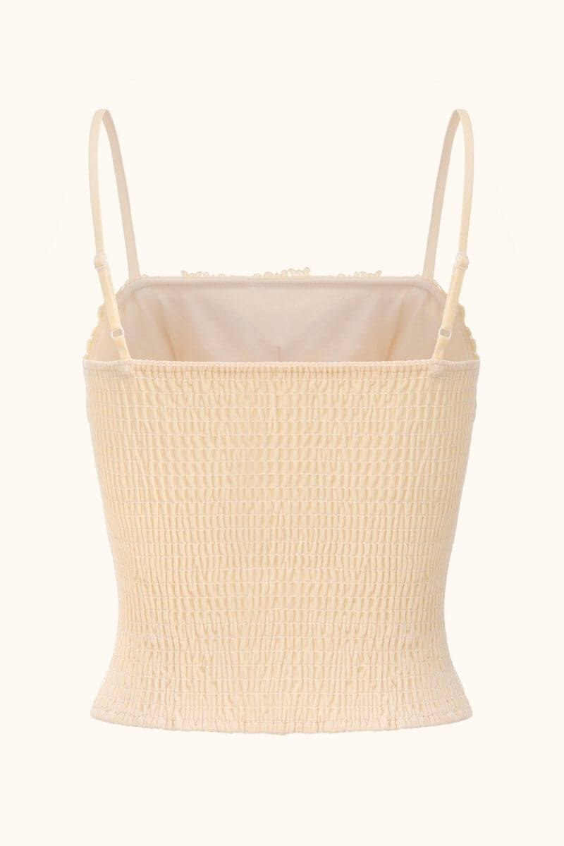 Back view of a beige satin corset top featuring smocked elastic paneling, slim adjustable straps, and soft lace-edged hem on white background.