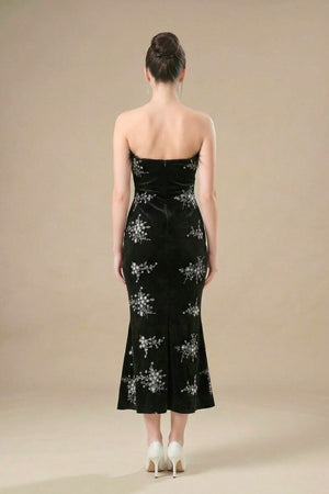 Back view of a strapless black velvet gown with silver floral embroidery, showing the fitted silhouette and floor-length hem.