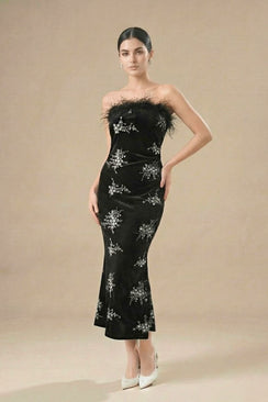 A woman in a black strapless velvet gown decorated with silver floral embellishments and a feather-trim neckline, posing elegantly in a studio.