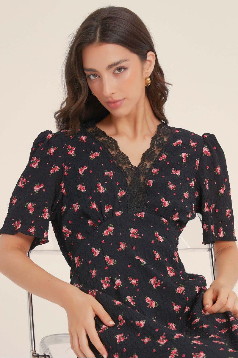 Close-up of a black floral dress featuring a scalloped lace V-neckline and puff sleeves, showing fine texture and intricate floral embroidery.