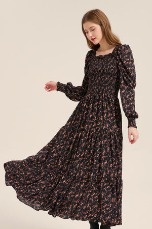Model twirling gracefully in a black floral puff sleeve maxi dress with a smocked bodice and tiered hem, showing the soft movement of the skirt.