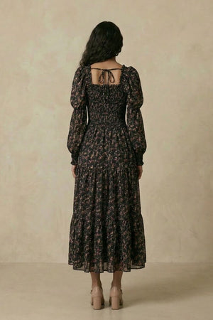 Back view of the black floral smocked midi dress highlighting the tie-back square neckline, puff sleeves, smocked waist, and tiered midi-length skirt.