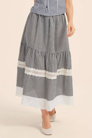 Close-up of a black gingham skirt with double lace bands and scalloped white hem, featuring a softly gathered tiered silhouette.