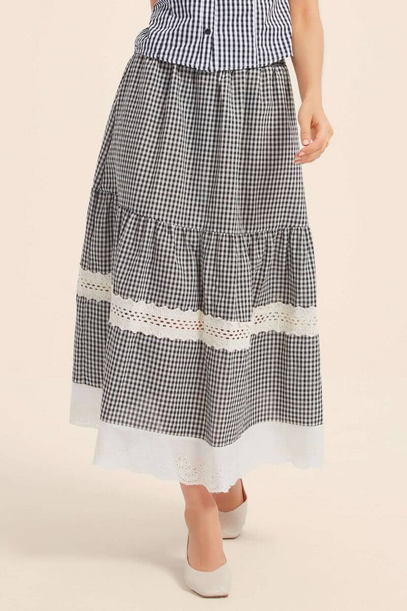 Close-up of a black gingham skirt with double lace bands and scalloped white hem, featuring a softly gathered tiered silhouette.