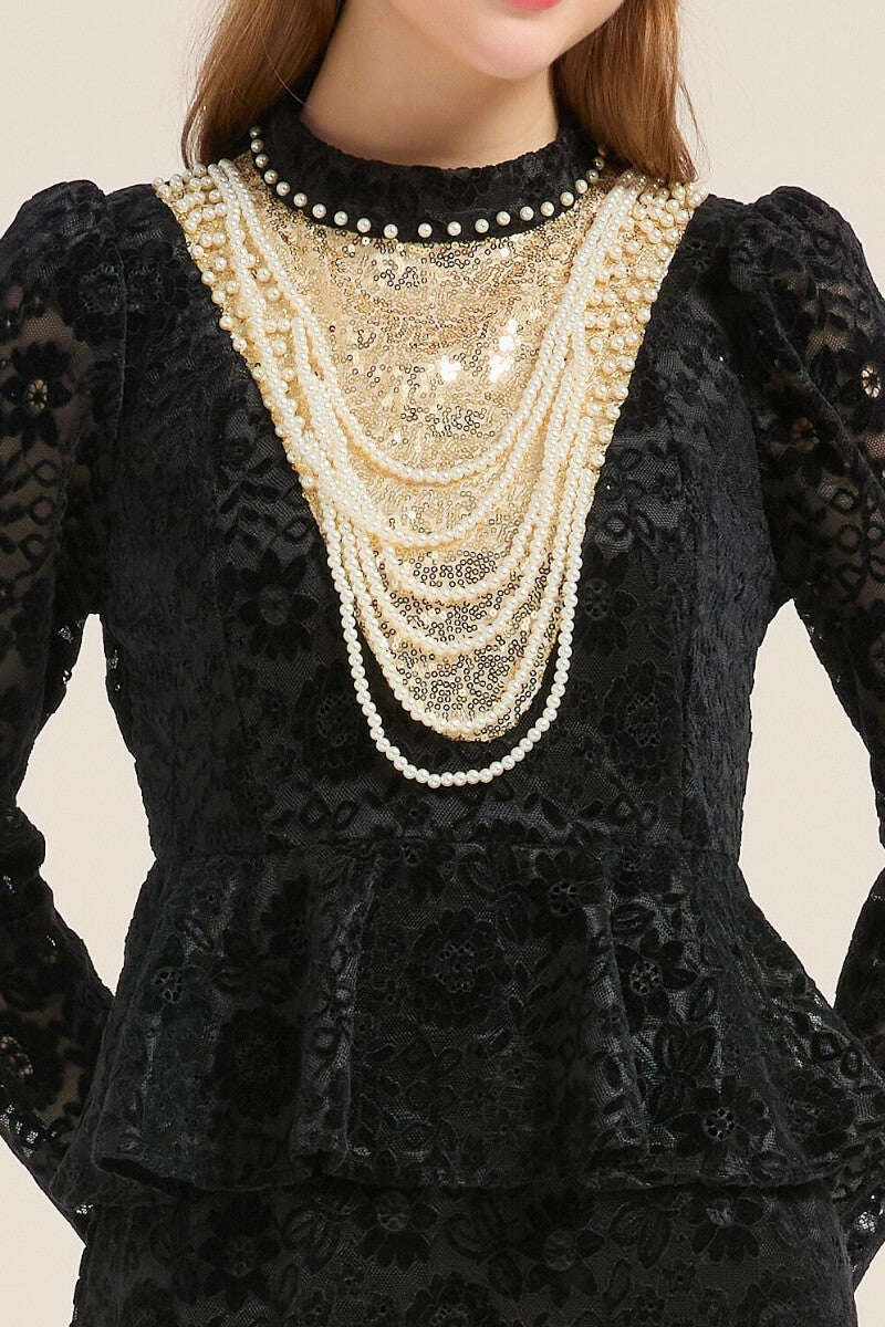 Close-up of a black lace peplum dress featuring gold sequin paneling and layered pearl embellishments around the neckline, highlighting its luxurious texture.