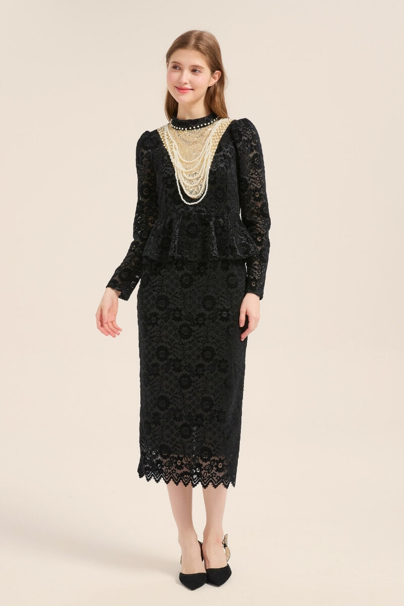 A woman wearing a black floral lace peplum midi dress adorned with layered pearl necklaces and long sleeves, styled with black pumps and a soft smile.