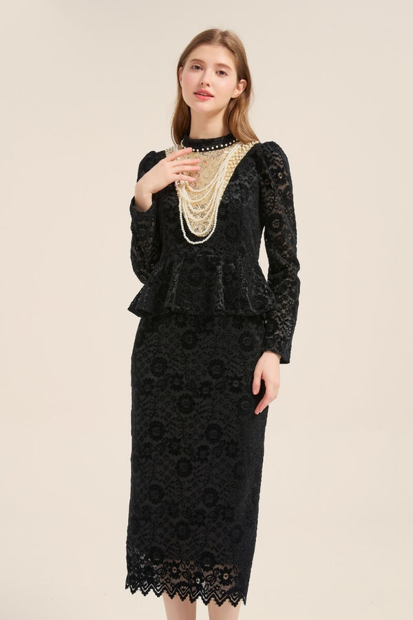 A woman wearing a black lace peplum midi dress featuring a high neckline with layered pearl embellishments, long sleeves, and a slim pencil silhouette, standing against a beige backdrop.