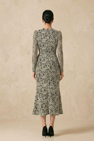 Back view of the black lace wrap midi dress showing the fitted waist, continuous lace pattern, and graceful midi-length hemline styled with classic heels.