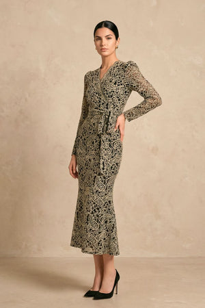 Model shown in side view wearing a black lace wrap midi dress with long sleeves and a gently defined waist tie, paired with black heels in a minimalist studio setting.