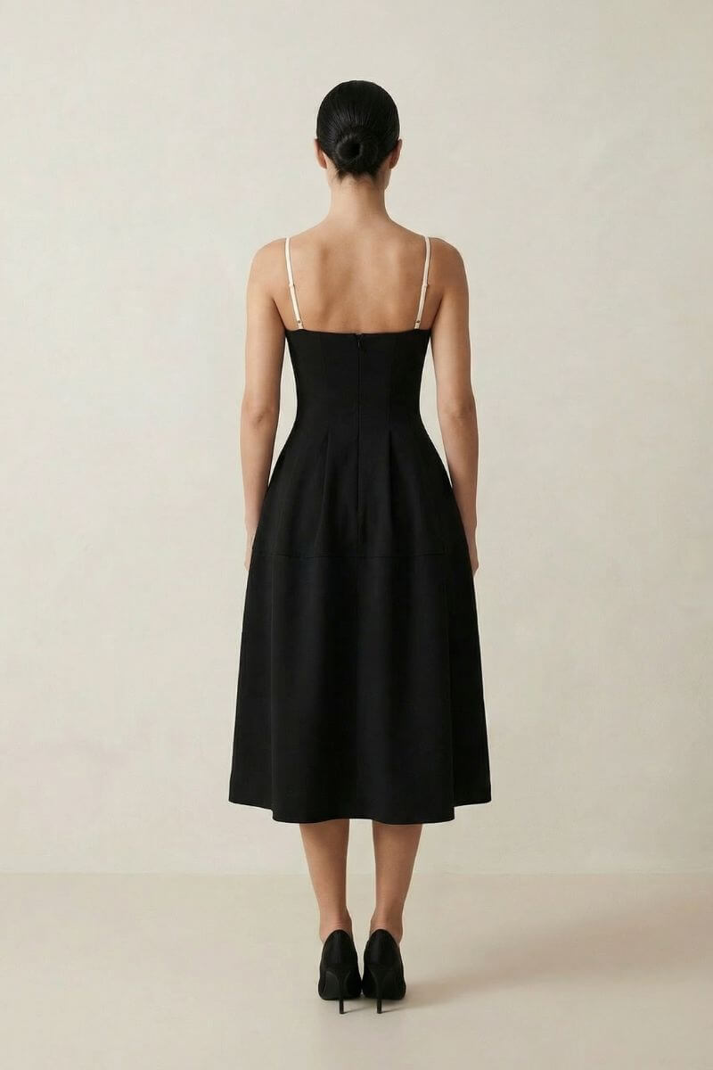 Back view of the black midi dress with adjustable ivory straps, a fitted waist, and a graceful A-line skirt shown against a neutral studio backdrop.