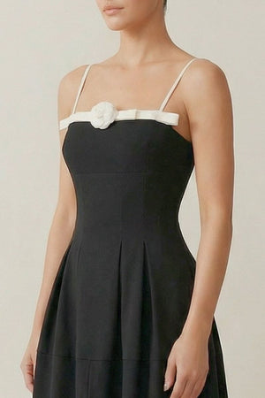 Close-up of the black midi dress showing the fitted bodice, ivory satin trim, and small white rosette accent across the neckline.