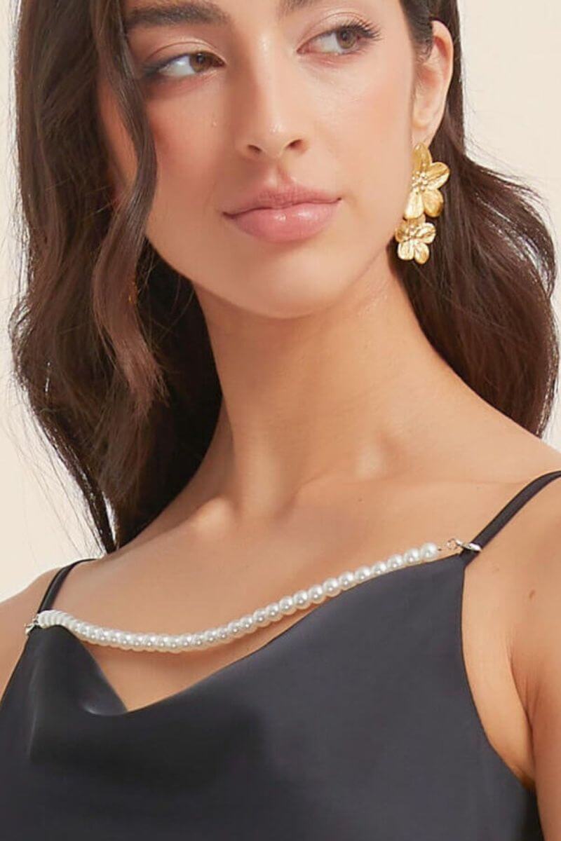 Close-up of a black satin slip dress showcasing its delicate pearl-trim neckline and slim straps, highlighting the refined sheen of the satin fabric.