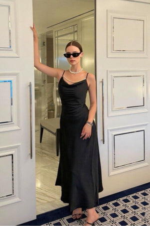 Woman styled in a black satin maxi dress with pearl neckline and strappy heels, accessorized with sunglasses and jewelry for a modern, glamorous evening look.