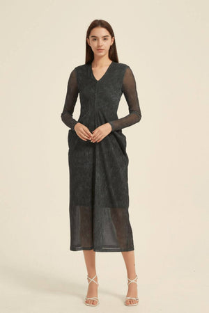 Model wearing a black midi dress with sheer sleeves, V-neck, subtle texture, front pleats, and a lightly sheer hemline.