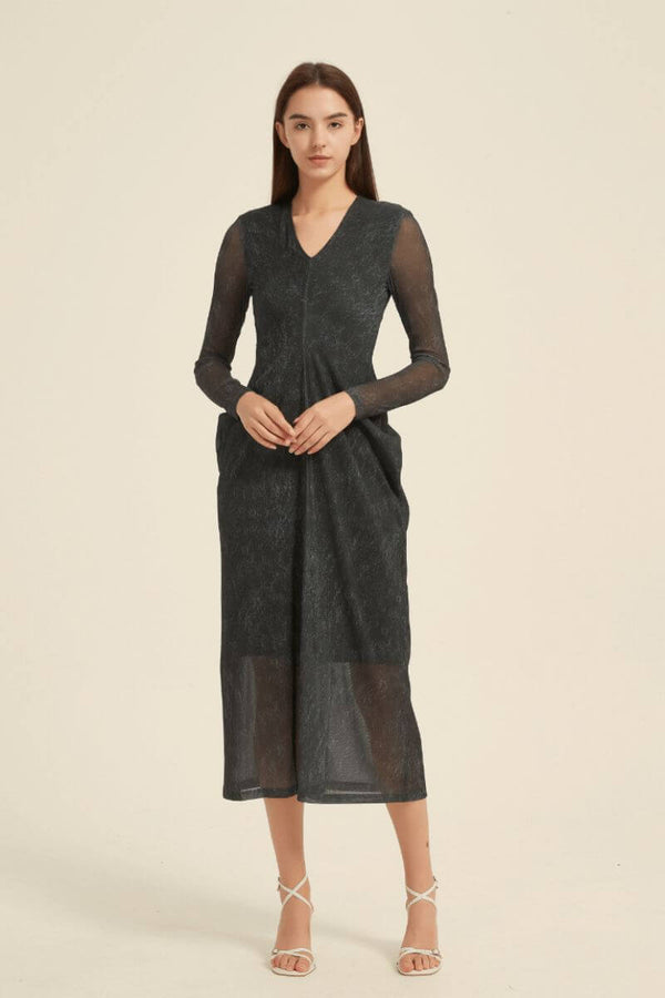 Model wearing a black midi dress with sheer sleeves, V-neck, subtle texture, front pleats, and a lightly sheer hemline.