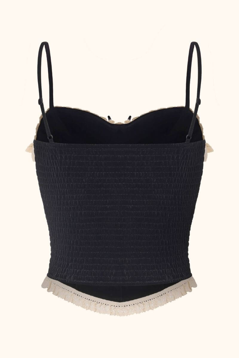 Back view of a black velvet corset top with stretchy smocked panel, adjustable thin straps, and cream lace edging, displayed on a white background for Sioéne.
