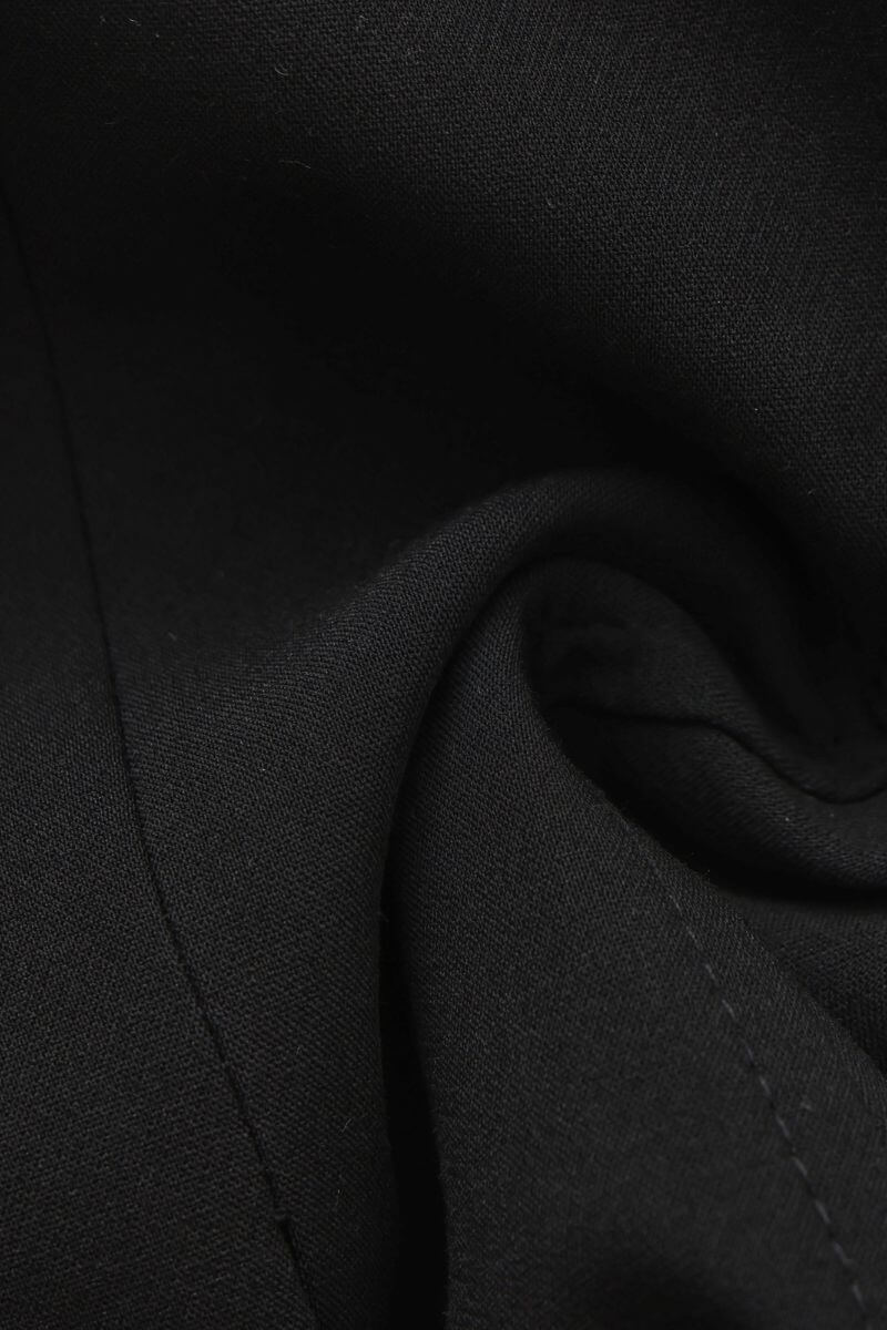 A close-up detail shot of black woven fabric with a soft, matte texture and visible stitching folds.