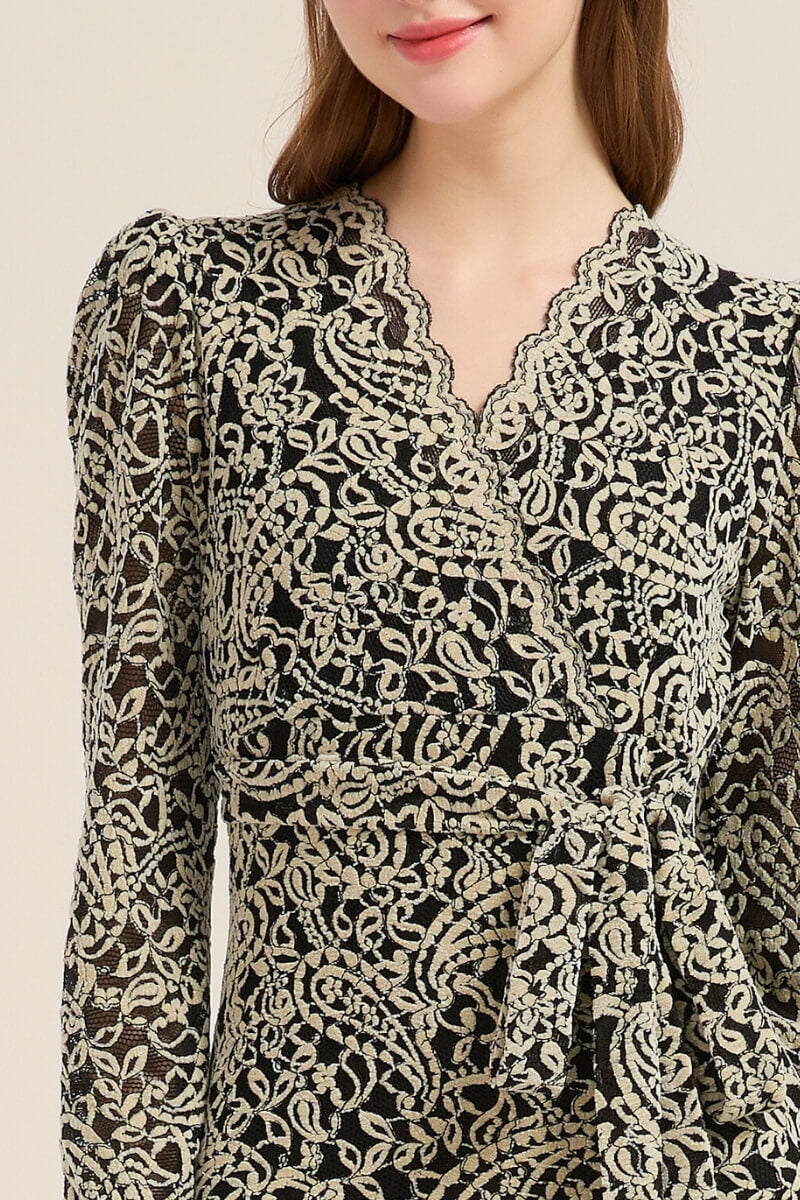 Close-up of a black and beige embroidered wrap midi dress showing its intricate floral lace texture and scalloped V-neckline, styled with soft lighting for a refined look.
