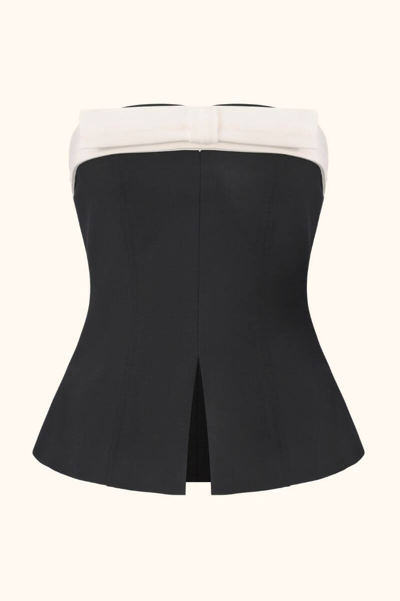 A black strapless top with a white bow trim shown from the back, highlighting its structured shape and center back slit.