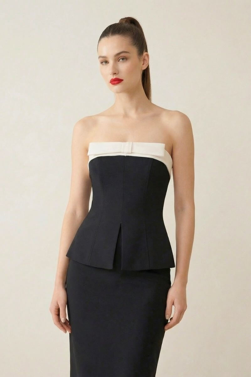 Model wearing a black strapless peplum top with white folded neckline paired with a black fitted midi skirt against a light studio backdrop.