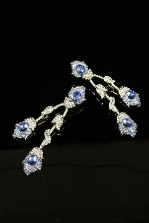 A pair of cascading drop earrings featuring faceted sapphire-blue crystals framed by clear rhinestones, arranged in a fluid vintage silhouette against a black background.