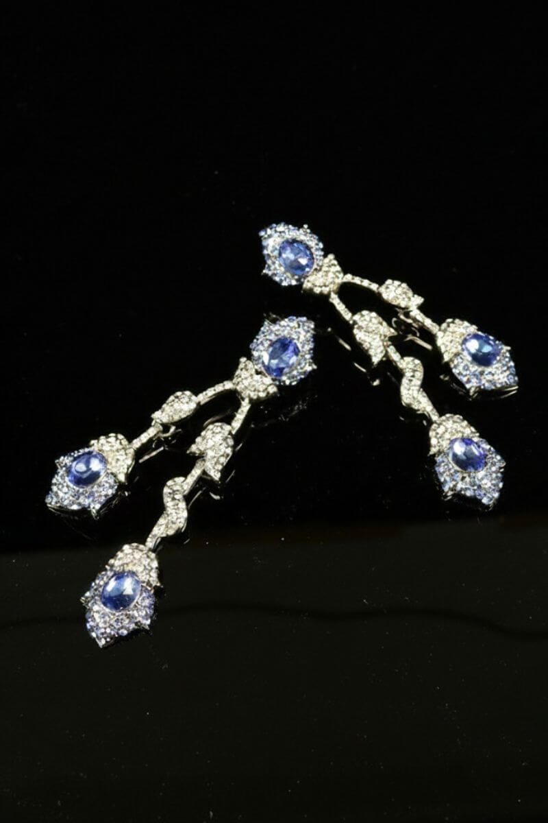 A pair of cascading drop earrings featuring faceted sapphire-blue crystals framed by clear rhinestones, arranged in a fluid vintage silhouette against a black background.