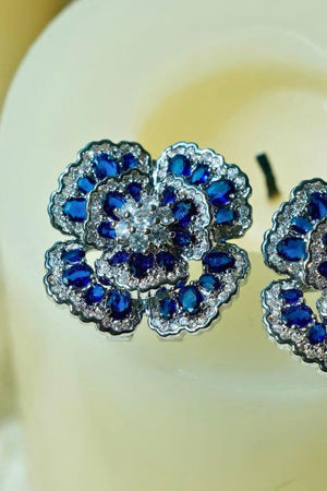 Detailed close-up of blue floral gemstone stud earrings showing the multi-layer flower structure, faceted blue stones, and sparkling clear accents.