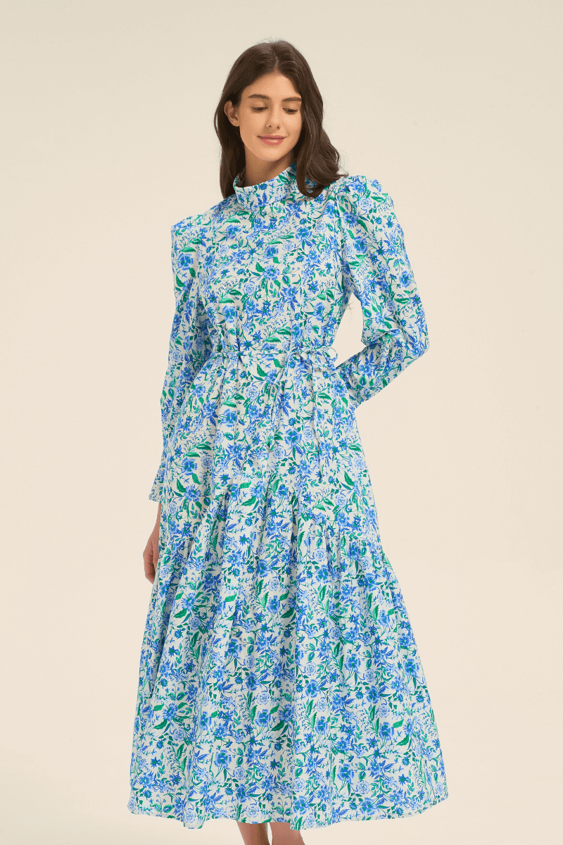 Model wearing a blue floral long sleeve midi dress with high neck and tiered skirt, front view.