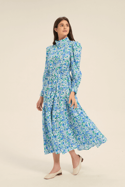 Model walking in a blue floral high neck midi dress with puffed shoulders and tiered skirt, side-front view.
