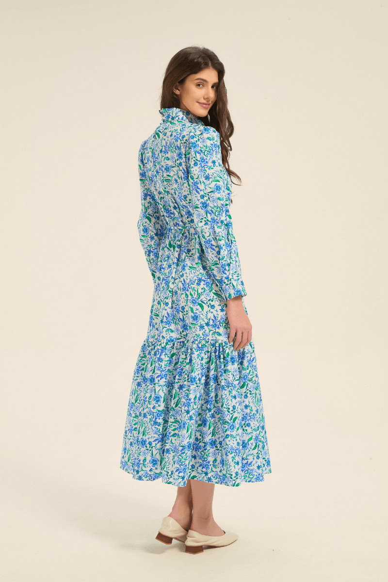 Side angle of model wearing a blue floral long sleeve midi dress with cinched waist and flowy skirt.