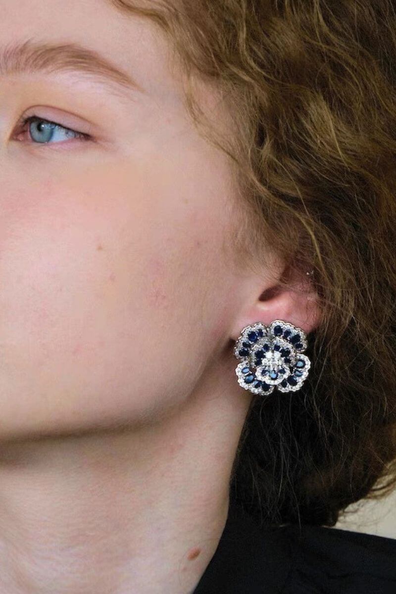 Natural light portrait of a model wearing blue floral gemstone stud earrings, emphasizing the layered petal design and luminous blue gemstones.