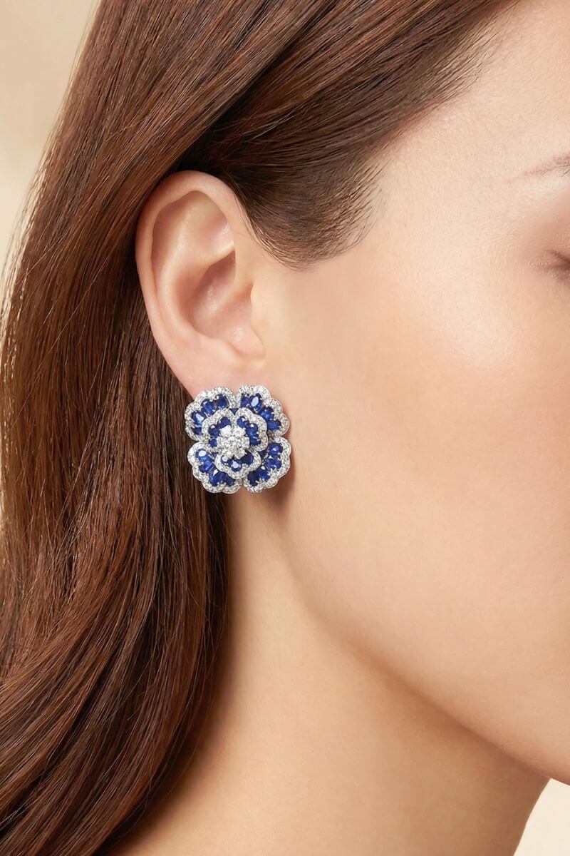 Side profile of a model wearing blue flower-shaped gemstone stud earrings with a silver-tone setting and multi-layered petal details.
