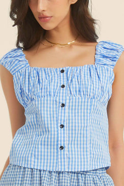 Close-up of a blue gingham sleeveless top with ruched straps and black buttons down the front, styled with gold jewelry.